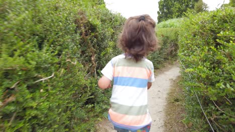 Baby-boy-with-long-hair-running-through-a-hedge-maze-in-slow-motion