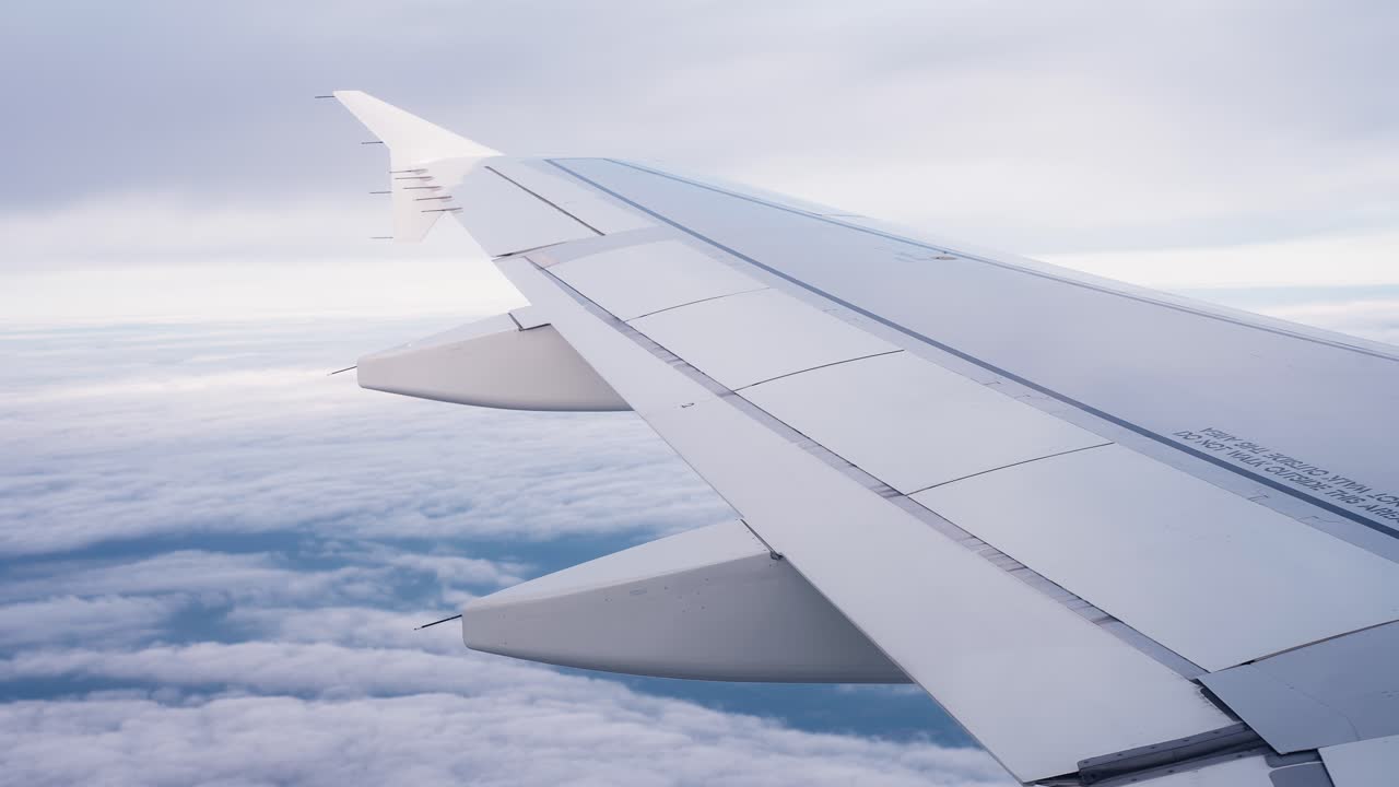 Vista dal finestrino di un passeggero di un'ala di aereo che scivola sopra un mare di nuvole luminose, catturando un volo di crociera tranquillo con tonalità di cielo tenui e serenità a cielo aperto
