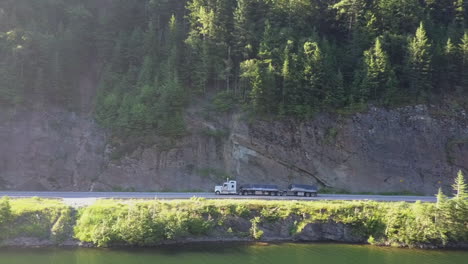 lens flare aerial pans left with mountain lakeside flatbed semi truck