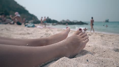feet with manicure on sandy beach with people close view