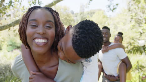 Mother carrying son on back, smiling while father carrying daughter in background
