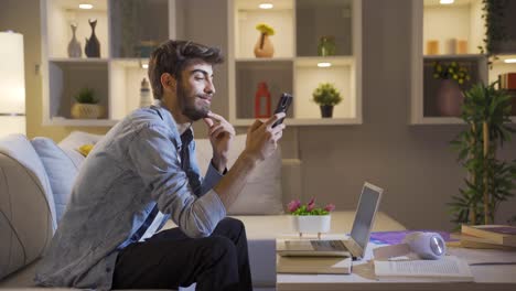 hombre usando las redes sociales en el teléfono riendo por la noche en casa.