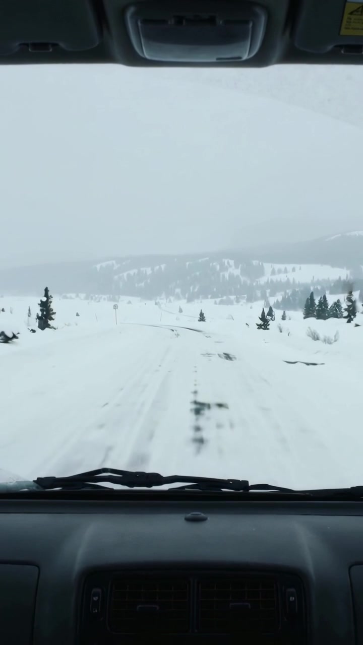 Vertical video: Ignition starting vehicle following ruts to navigate snowy pass, windshield visible