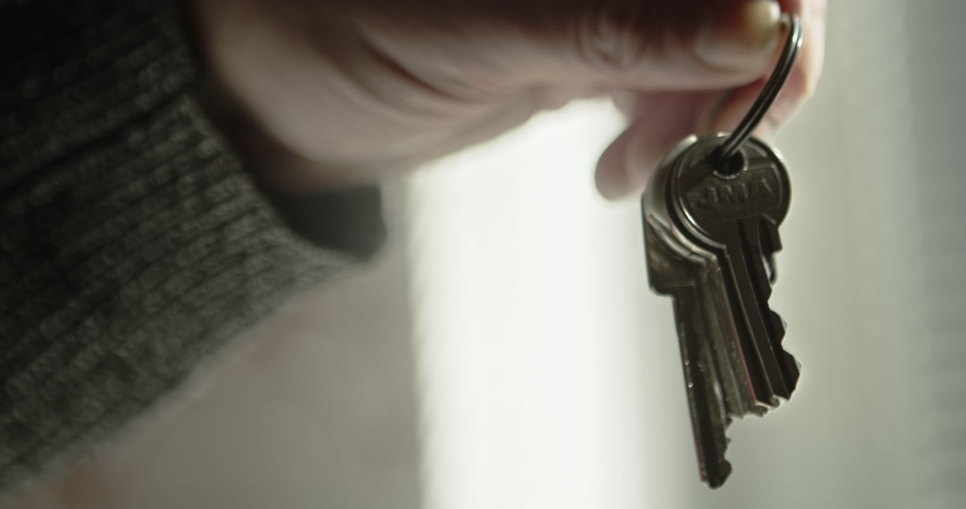 Arm dangling a set of doorkeys on a keyring in a bright room. Perfect for housing market news, rental agency promos, and moving day content.