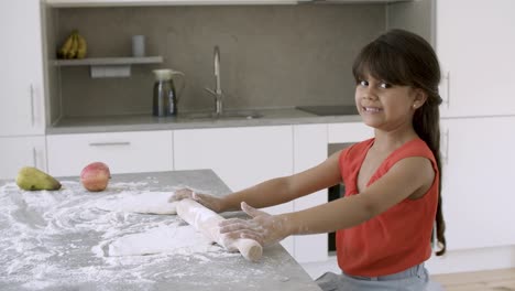 adorable niña rodando la masa en la mesa de la cocina