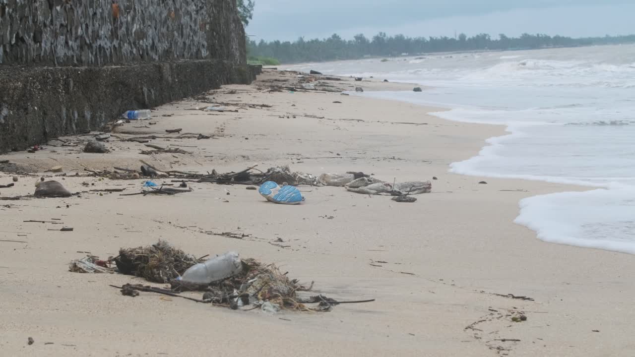 Olas rompiendo en una playa de arena cubierta de basura plástica y escombros - vista amplia