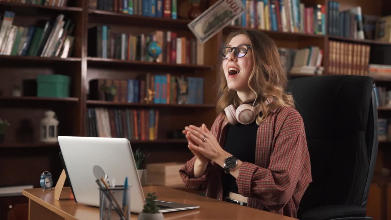 la chica está sentada en una silla, trabajando en su portátil, cuando de repente el dinero comienza a caer desde arriba