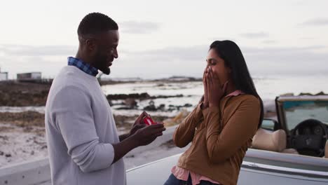 Hombre-Afroamericano-Proponiendo-A-Su-Novia-Con-Un-Anillo-Cerca-Del-Auto-Convertible-En-La-Carretera