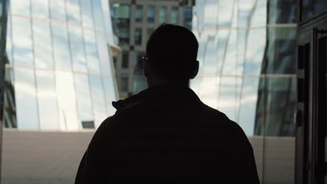 unrecognizable man walking past glass buildings