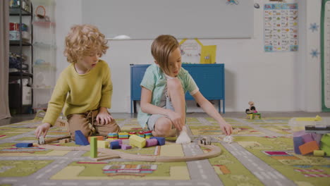 front view of two little boys playing with wooden pieces and car sitting on a carpet in a montessori school class