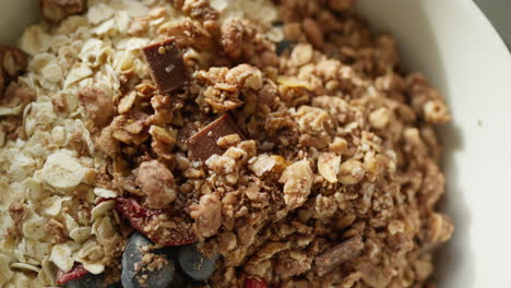 close-up of a breakfast bowl with granola, chocolate, and berries on a table