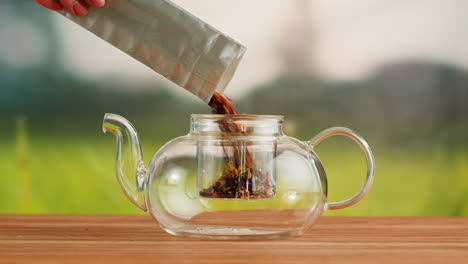 pouring loose leaf tea into a glass teapot