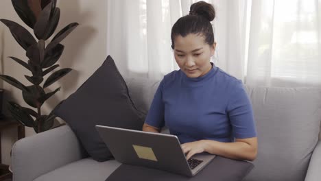 New-normal-businesswoman-work-from-home-by-laptop-sitting-on-the-sofa-happily