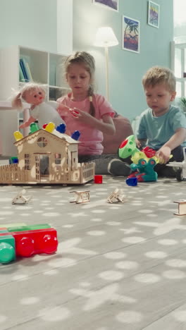 los niños juegan con la muñeca bebé y el avión sentados cerca de la casa de madera. niña y niño pasan tiempo en la vista de la guardería a través de la autorización en la construcción de cubos