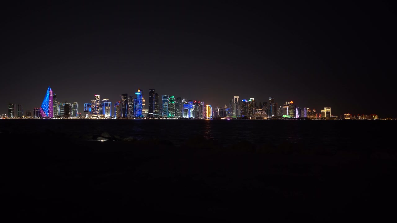Fantastisk panoramautsikt over den opplyste Doha West Bay-skyline om natten. De livlige neonlysene fra Qatars moderne skyskrapere reflekteres over det mørke vannet i Persiabukta.
