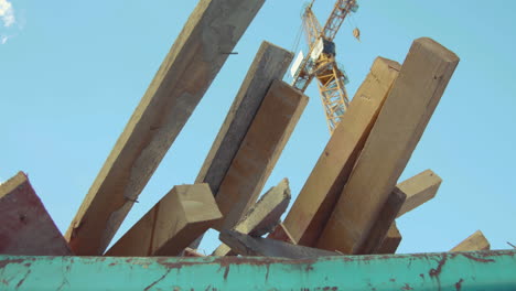 troncos de un sitio de construcción sobresalen de un contenedor con una grúa de construcción en el fondo