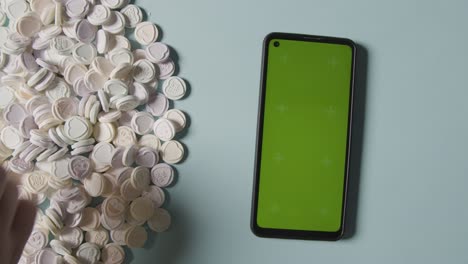 person choosing from pile of heart candy with romantic messages of love next to green screen mobile phone