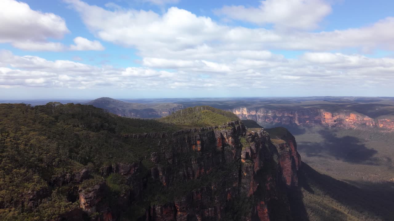 Slow drone orbit revealing expansive tree-covered slopes and distant rugged peaks in warm light, steep bare escarpment, Blue Mountains NSW Australia