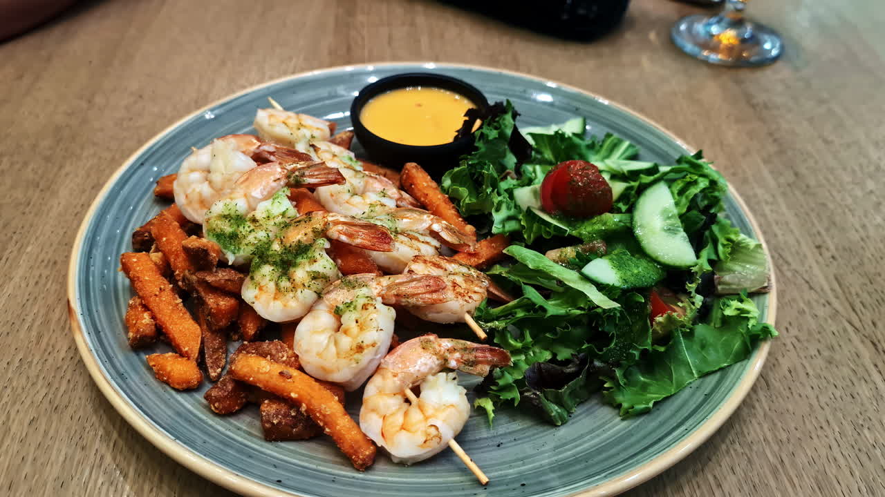Skewered shrimp served with sweet potato fries, mixed greens, cucumbers, and dipping sauce