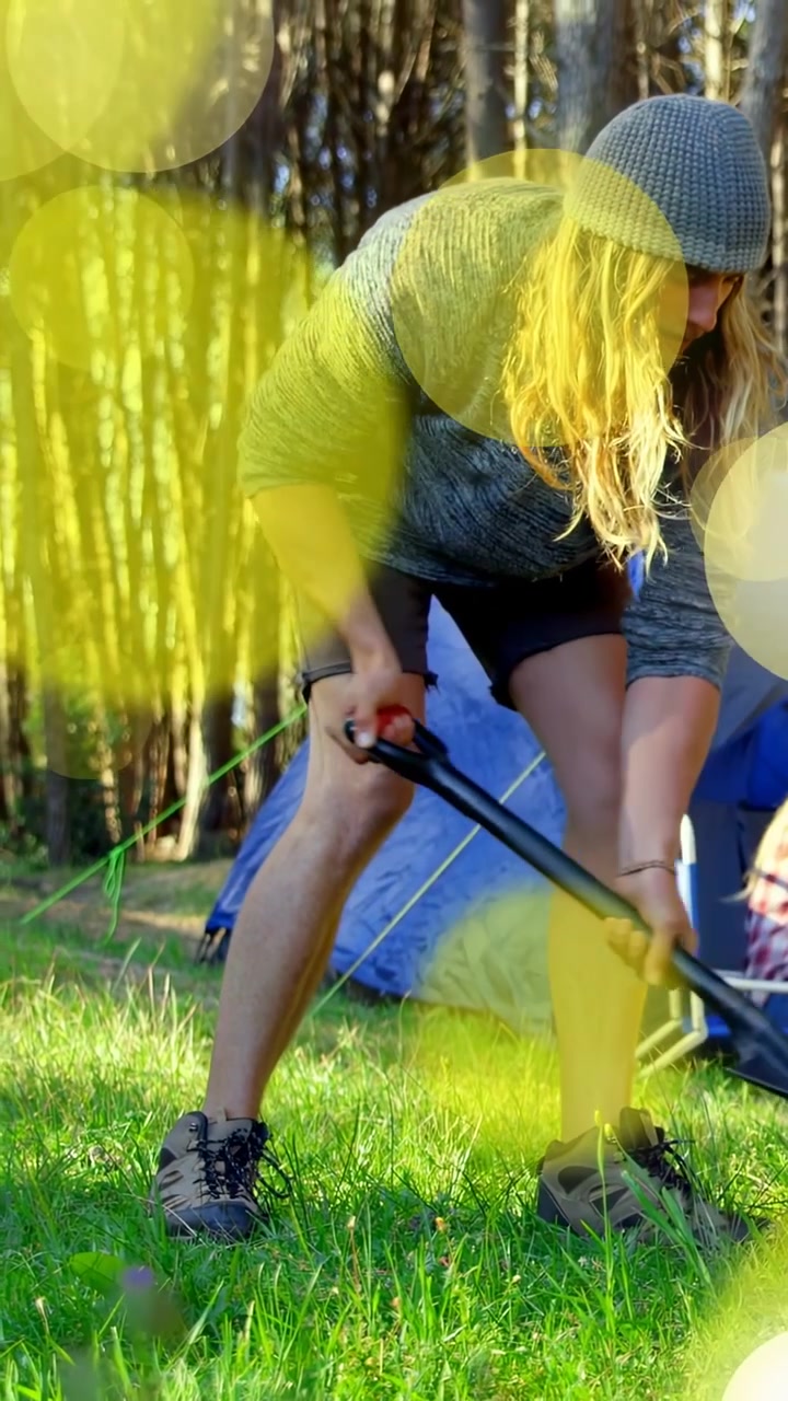 Verticale video: Kampeerder pakt gereedschap en wrikt haringen los, zet tent vast op de camping, gouden bokeh zweeft.