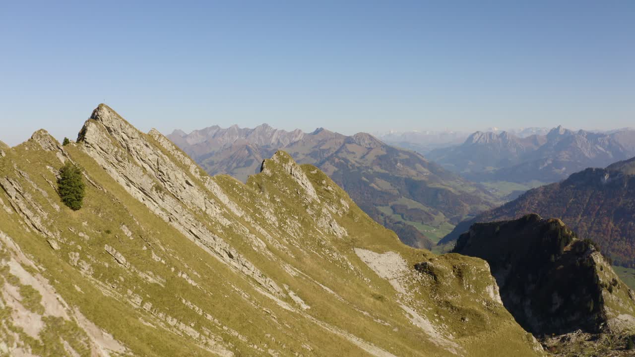 vuelo bajo sobre un empinado paso de montaña con los alpes al fondo, colores otoñales
