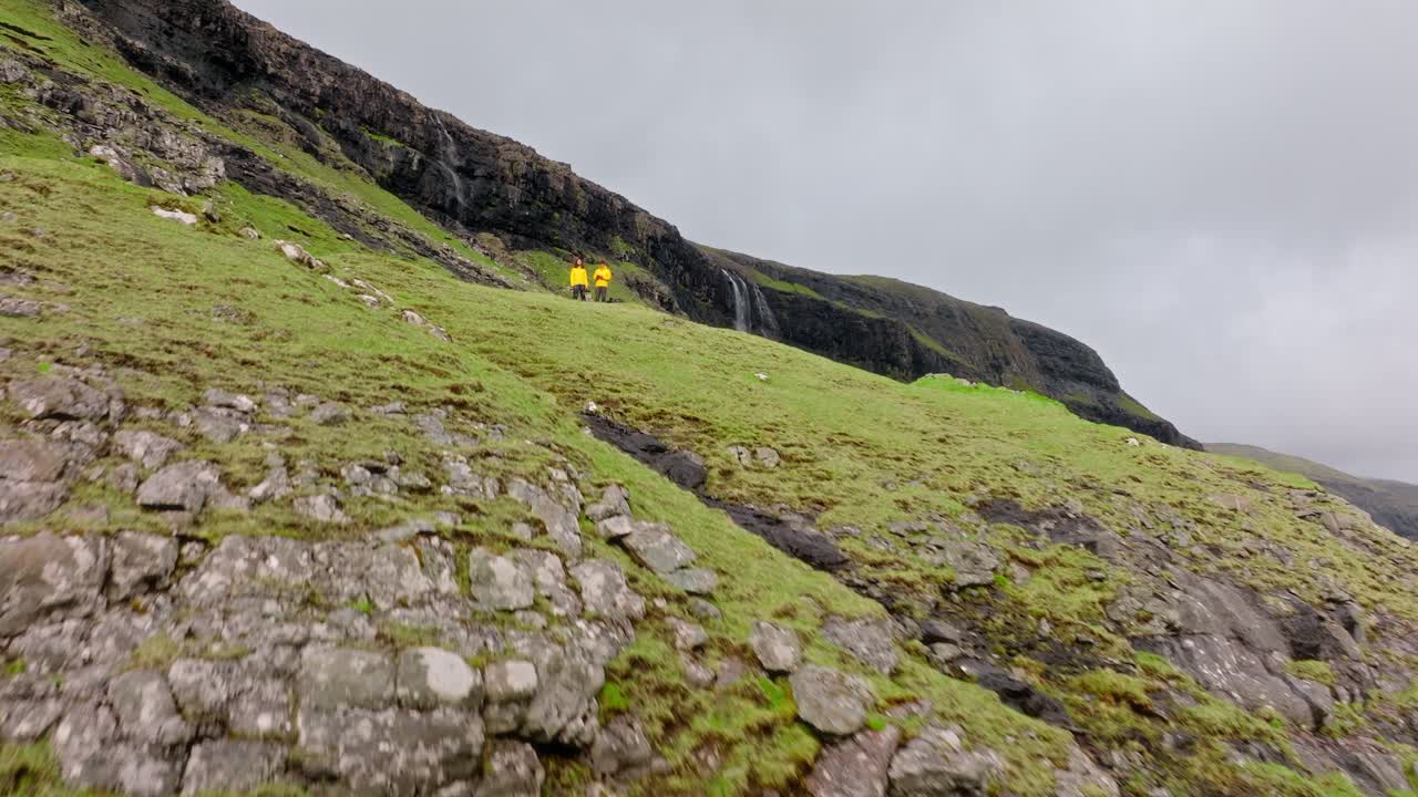 A rugged Faroe Islands cliffside, with hikers in bright jackets and overcast skies