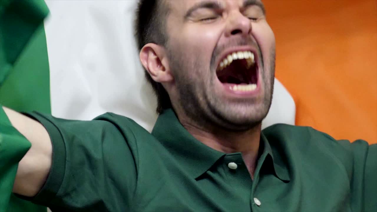 fanático irlandés celebrando mientras sostiene la bandera de irlanda en cámara lenta, 4k, de alta calidad