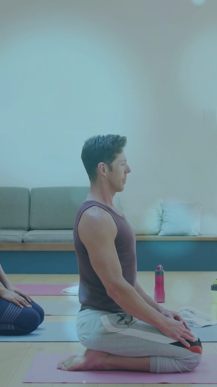 Vertical video: Cueing man kneeling on pink mat, keeping yoga pose for calm as bokeh crossing frame