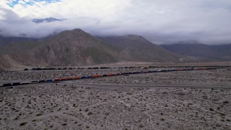 Aerial-Drone-Footage-of-Cargo-Train-in-Palm-Springs-Desert-with-mountains-in-the-Background,-slow-moving-wide-shot-forward