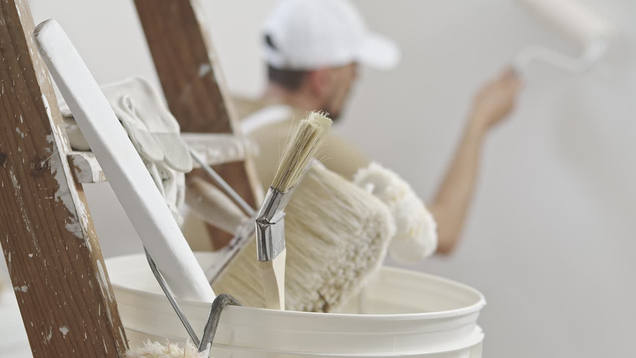 집 화가의 손, 장식가, 집을 리모델링하는 일, 롤러 페인트를 사용하고  버을 들고, 뒷면으로 페인트 브러쉬를 가진 나무 사다리, 클로즈업