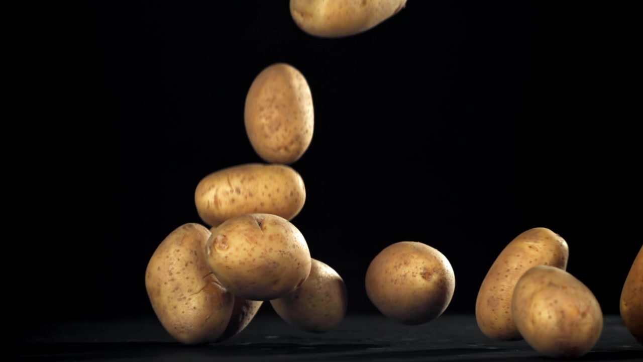 Patate crude che cadono al rallentatore su uno sfondo nero.