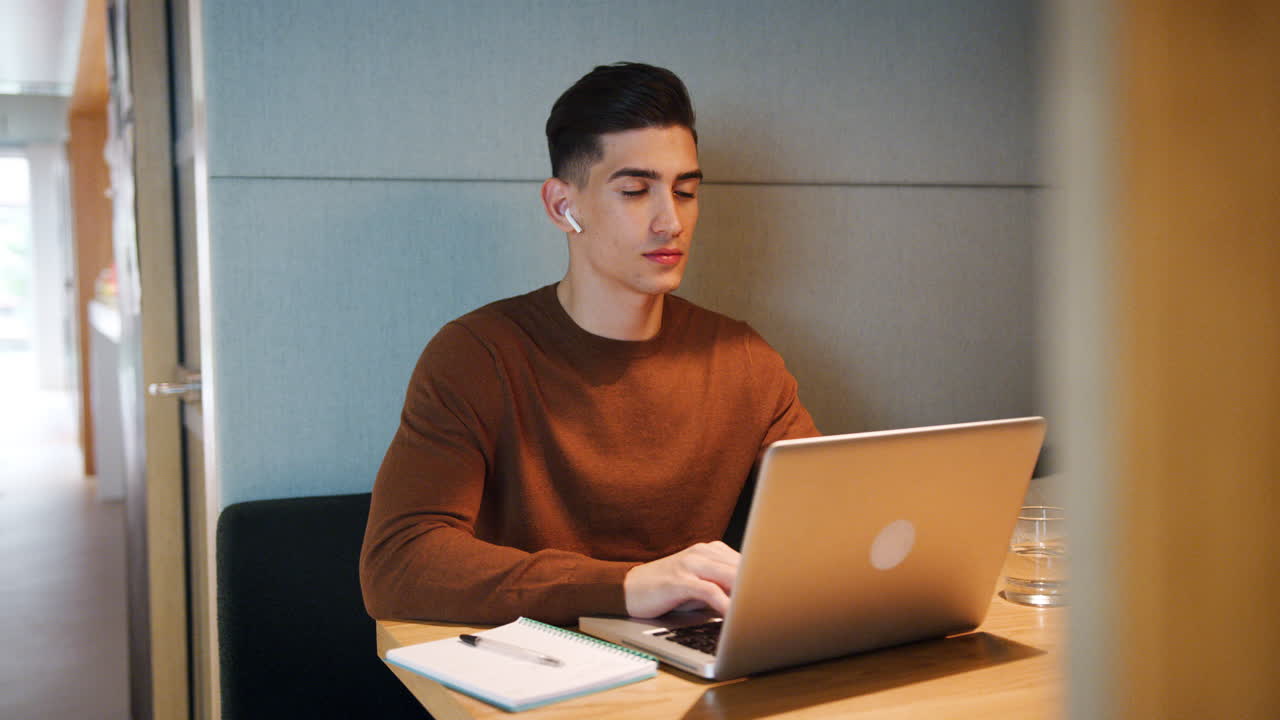 joven trabajando solo en una computadora portátil en una mesa en una cabina en una cantina de oficina, enfoque selectivo