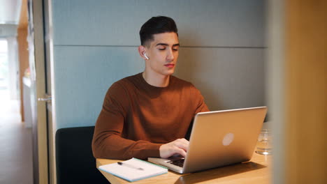 Young-man-working-alone-on-a-laptop-at-a-table-in-a-booth-at-an-office-canteen,-selective-focus