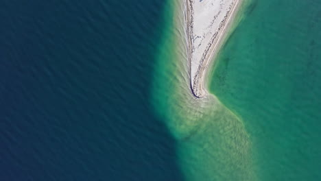 Drone-shot-looking-down-on-a-sand-bar-just-under-the-surface-of-the-water-that-connects-to-a-raised-sand-reef