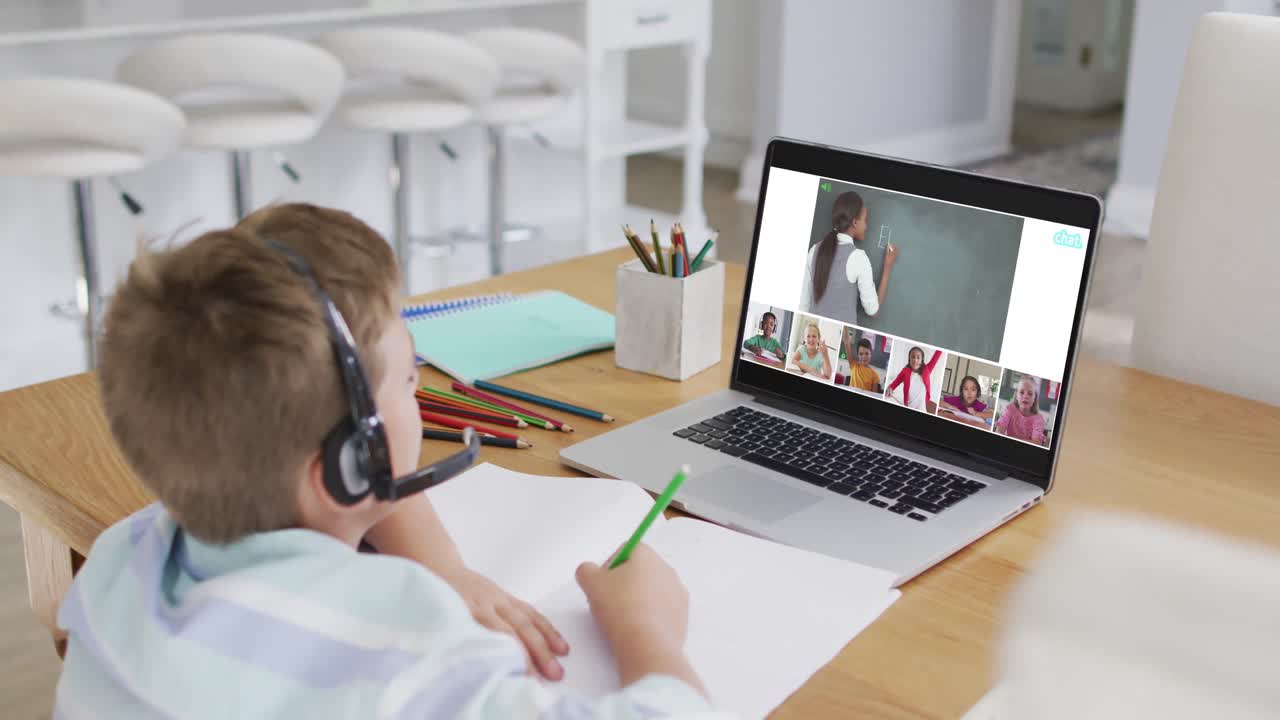 Schoolboy using laptop for online lesson at home, with diverse teacher and class on screen