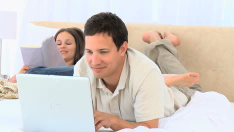 hombre feliz trabajando en la computadora mientras su esposa está leyendo un libro