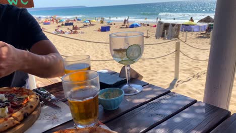 enjoying two pizzas and drinks at the beach with a beautiful sea view in lisbon portugal, restaurant in summer on a sunny day with blue sky, 4k shot