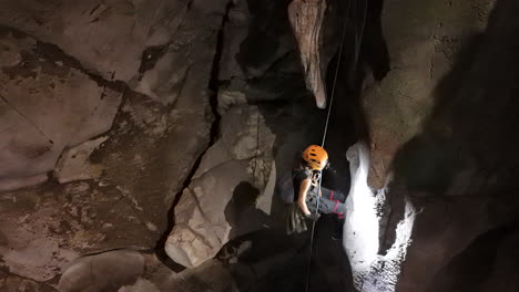 a caver uses the single rope technique (srt) to descend into the dark and mysterious anxiety state cave in chiang mai, headlamp illuminating the textured rock walls.