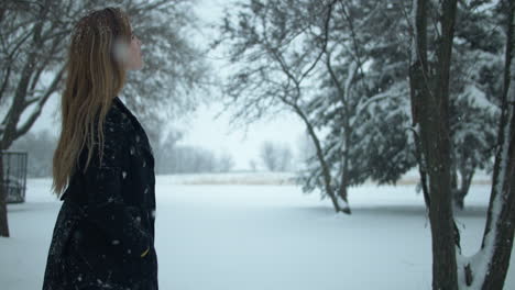 mujer caminando afuera en cámara lenta, viendo la nieve de invierno de navidad mientras los copos de nieve caen en cámara lenta cinematográfica