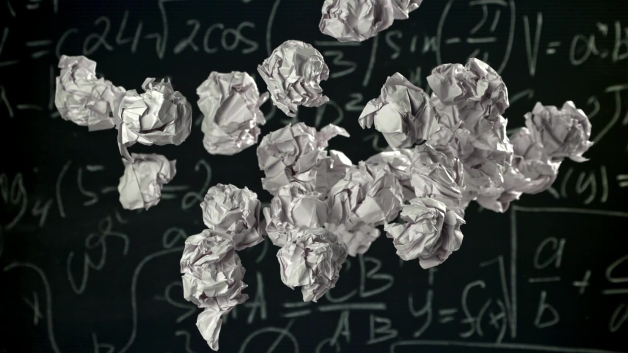 Boules de papier froissées flottant devant un tableau noir de mathématiques.