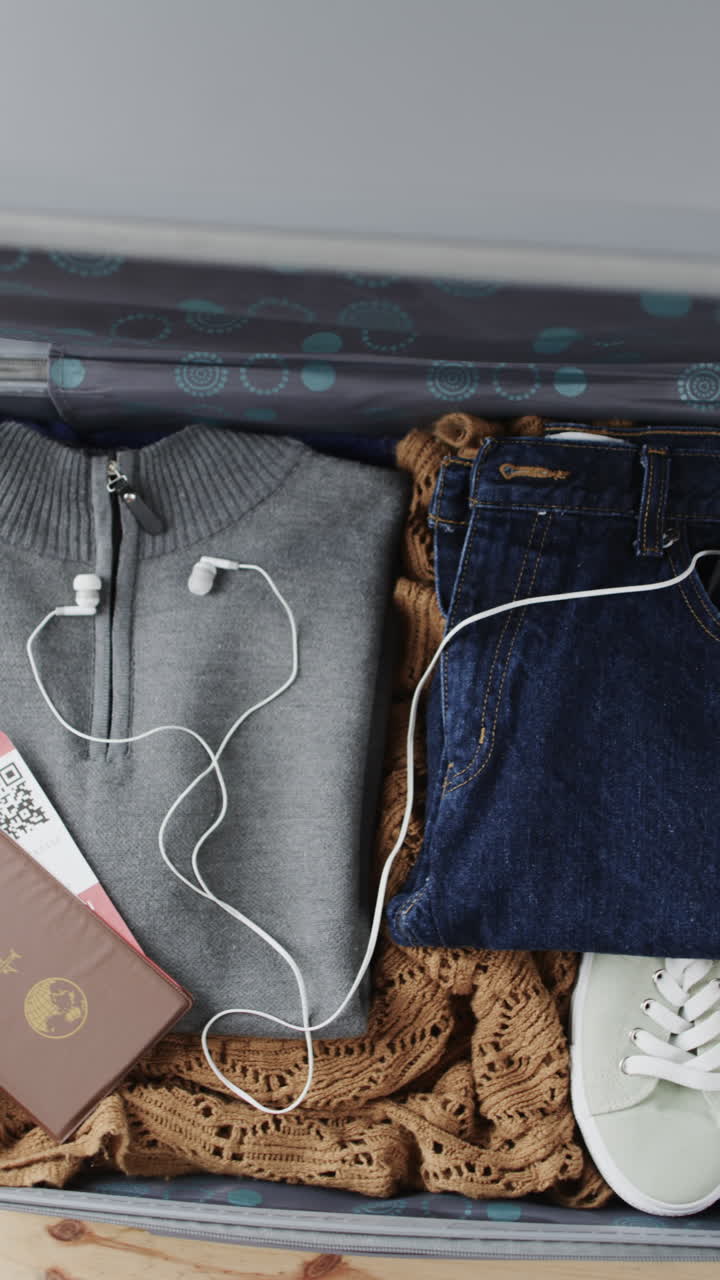 Vertical video of suitcase with travel clothes and passport on wooden background