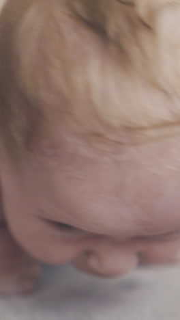 adorable newborn boy with large blue eyes and plump cheeks lies on stomach and enjoys back massage extreme close view