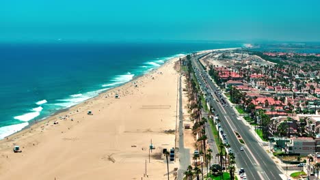 Aerial-view-over-Huntington-Beach-with-almost-no-people-and-some-large-waves-breaking-on-the-shore-and-just-a-few-cars-driving-down-pacific-coast-highway