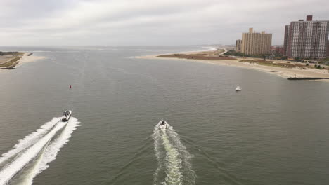 an aerial view over east rockaway inlet as two boats speed by leaving a white wake behind