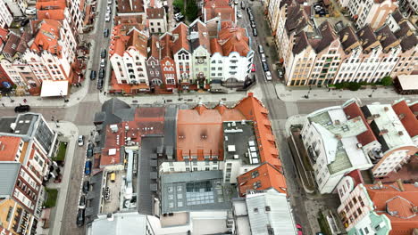 Vista-Aérea-Del-Centro-Histórico-De-Elbląg-Con-Sus-Distintivas-Y-Coloridas-Casas-En-Hilera-Y-Techos-De-Terracota,-Calles-Que-Se-Cruzan-Y-Autos-Estacionados.