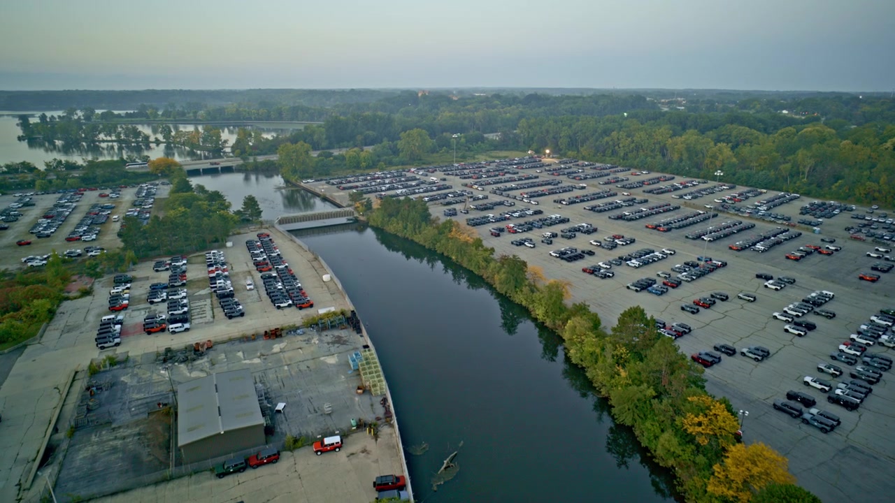 Drohnenaufnahmen einer Drohne, die über den Huron River fliegt, umgeben von neuen Autos, die auf einem Parkplatz in der Nähe von Ypsilanti, Michigan, auf Halbleiter warten.