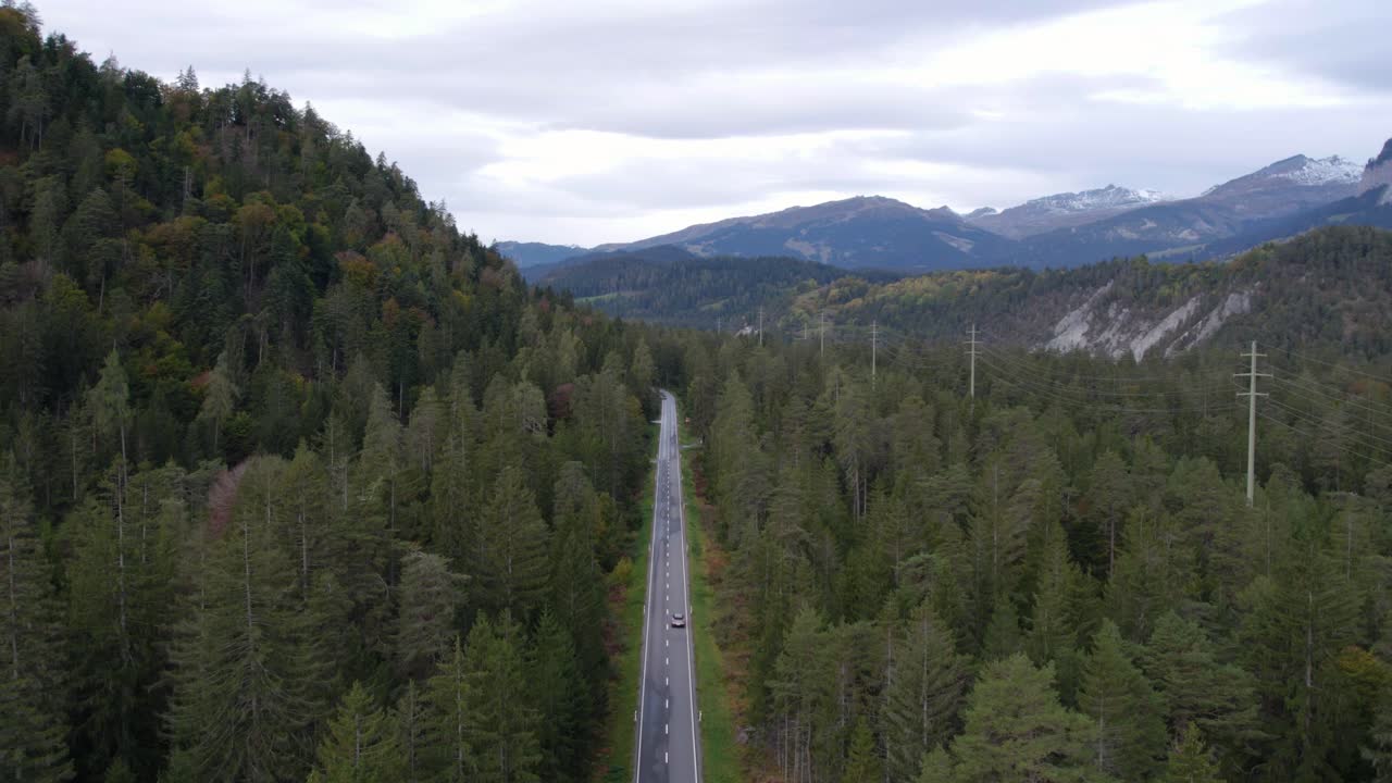 vista aérea de drones de un coche eléctrico conduciendo por una carretera alpina, en suiza nublada