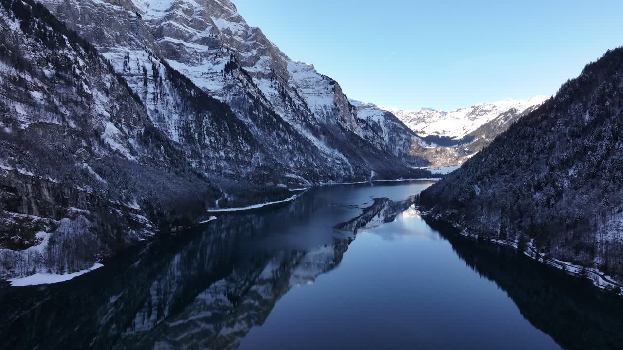 Aerial frozen Klöntalersee reflecting snowy Alps in Klöntal, Switzerland, serene winter