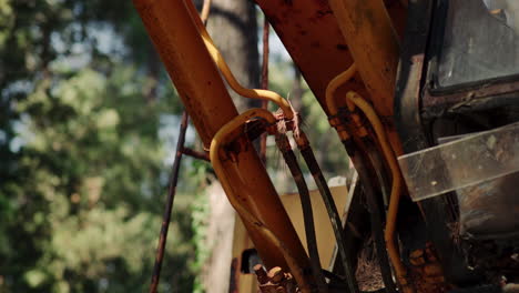 static view of decrepit heavy machinery in shadow of trees, detail shot of yellow weathered metal