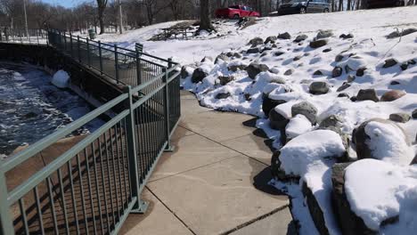 walking along sidewalk with river on one side and rocks covered in snow on the other side.